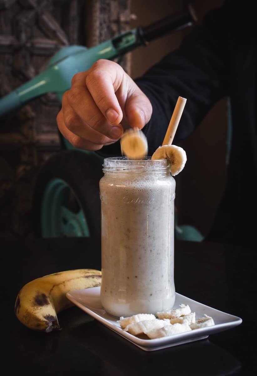 Person wirft ein Stück Banane in einen Proteinshake.