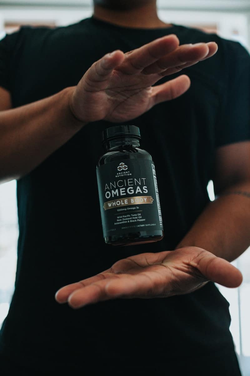 Eine Flasche mit Omega-3 Kapseln schwebt zwischen zwei Händen.